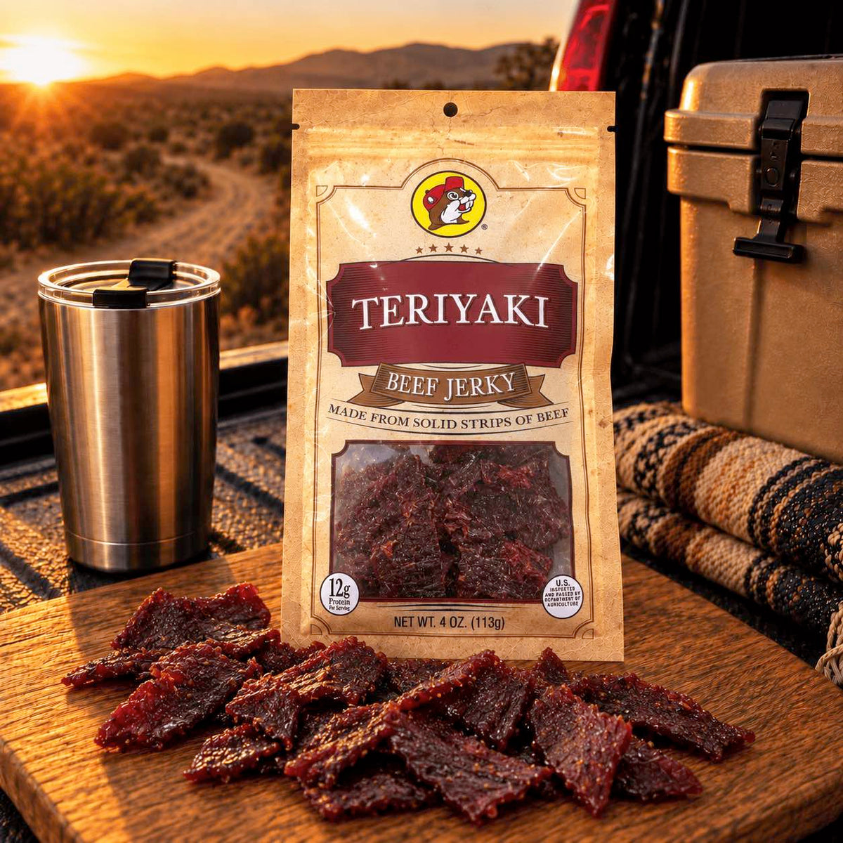 A bag of Teriyaki Beef Jerky is displayed on a wooden cutting board with several pieces scattered in front, set outdoors near a stainless steel tumbler, cooler, and a sunset landscape.